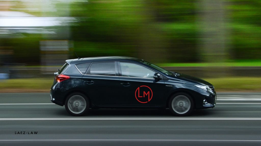 Coche negro en movimiento con logotipo rojo en la puerta, representando el tema de los gastos deducibles para autónomos en una inspección fiscal.